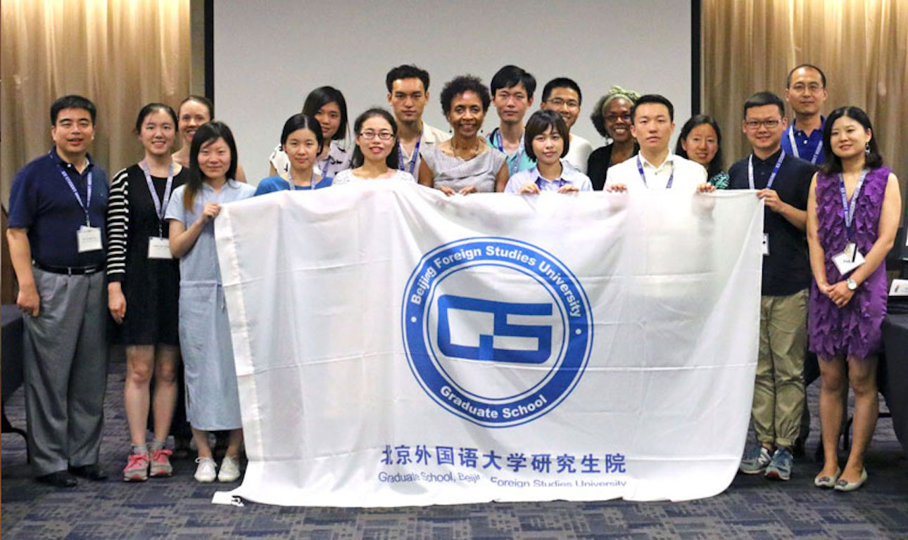 Scholars from Beijing Foreign Studies University (BFSU) alongside KU Chancellor Bernadette Gray-Little pose while holding the BFSU flag.