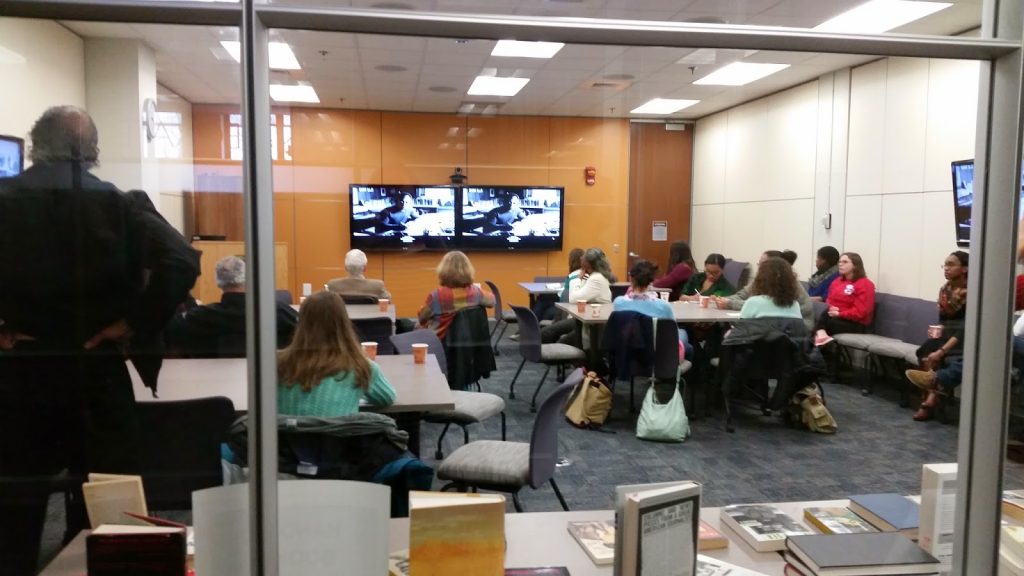 "An audience gathered in a small conference room"