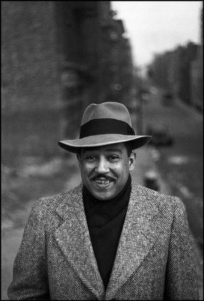 "A black and white image of a man in a blazer and hat"