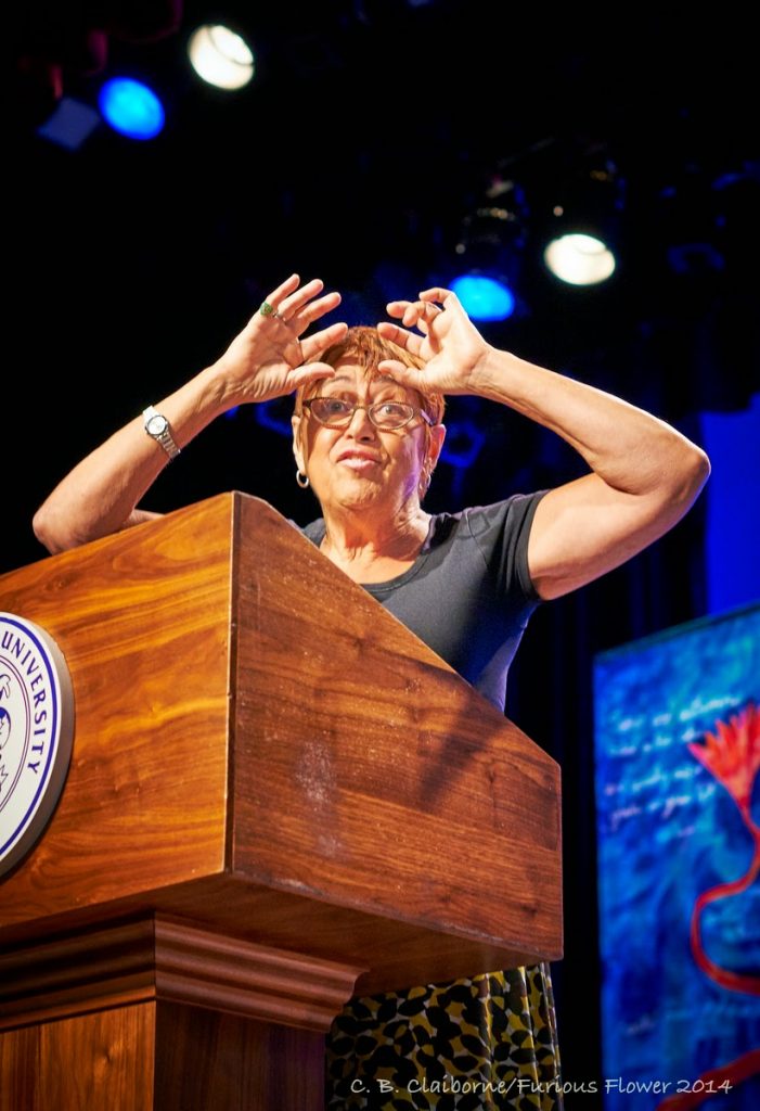 "A woman speaking at the podium while laying her hands on her forehead"