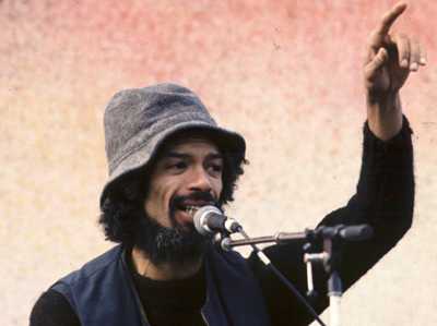 "Gil Scott-Heron wearing a grey bucket hat while singing into a mic "