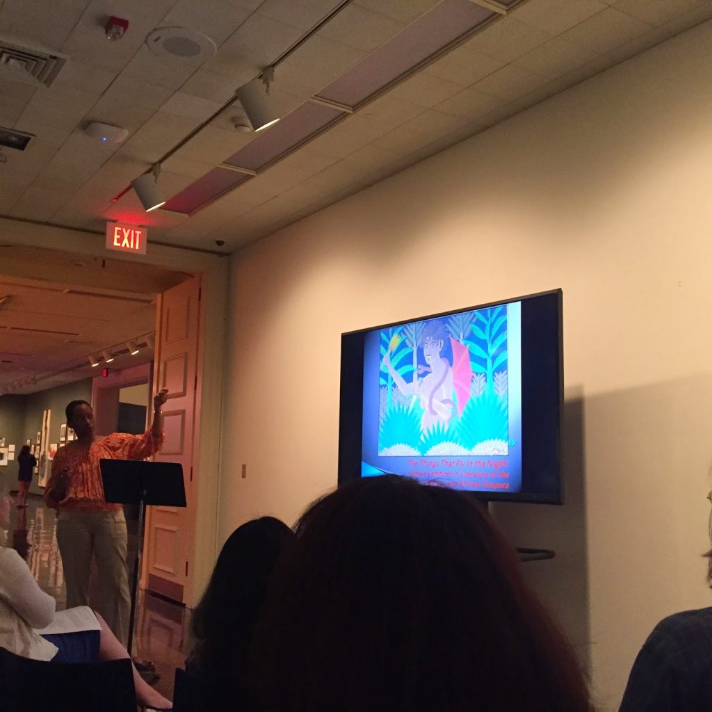 "Giselle Liza Anatol presenting her book displayed on a TV in a small conference room to an audience"