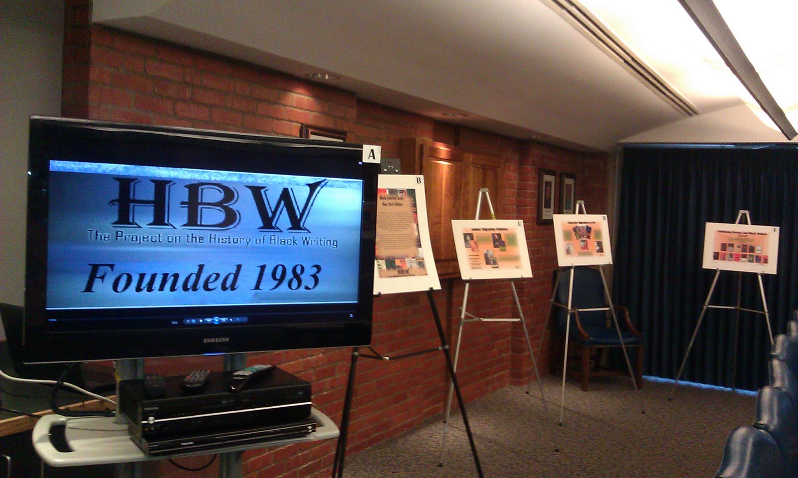 "An exhibition room with a TV displaying 'HBW: The project on the History of Black Writing. Founded 1983' "